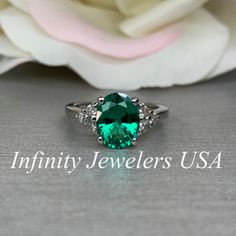 a green ring sitting on top of a table next to a white rose with the words infinity jewelers usa written below it