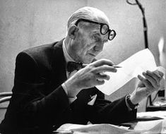 an old man sitting at a desk in front of a lamp reading a piece of paper