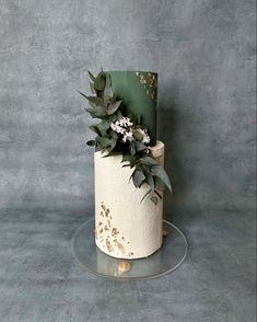 a three tiered cake decorated with flowers and greenery on a glass platter