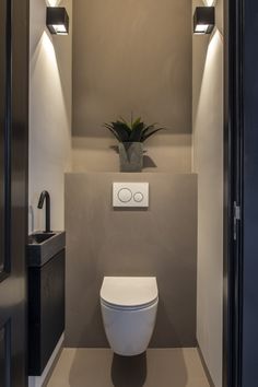 a toilet in the middle of a bathroom with lights above it and a plant on the wall