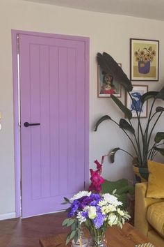 a living room filled with furniture and a purple door next to a table full of flowers