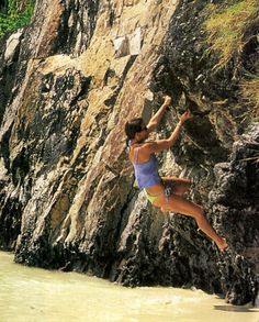 a woman climbing up the side of a cliff on a surfboard in the water