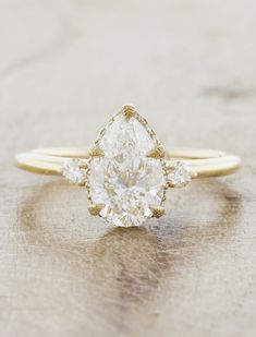 a pear shaped diamond engagement ring on a wooden surface with the top half in yellow gold