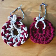 two red and white crocheted ornaments hanging from strings on a wooden table top