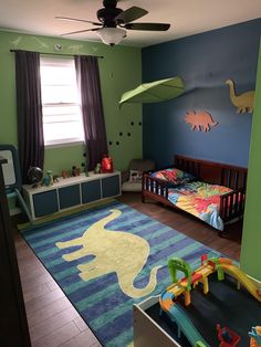 a child's bedroom decorated in green, blue and yellow with dinosaurs on the rug