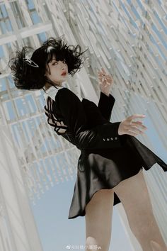 a woman with black hair is posing in front of a white structure wearing a short skirt and jacket