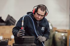 a man wearing headphones and holding a tool in his hand while standing next to a black object