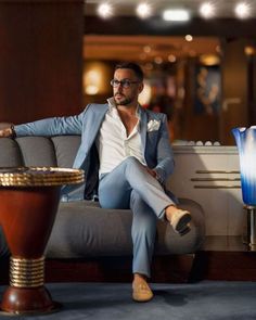 a man sitting on top of a gray couch next to a blue vase and table