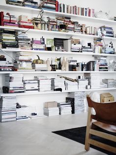 a room filled with lots of books on shelves next to a wooden chair and table