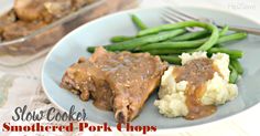 a white plate topped with meat covered in gravy next to green beans and mashed potatoes