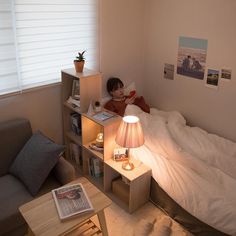 a young boy laying in bed reading a book next to a table with a lamp on it