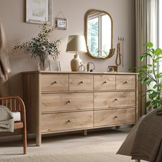 a bedroom scene with focus on the dresser and bed sideboard, potted plant and mirror