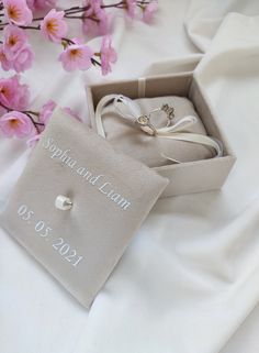 two wedding rings sitting in a box next to pink flowers on a white cloth covered table