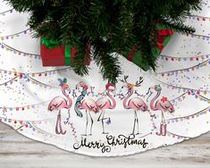 three pink flamingos are standing in front of a christmas tree with presents on it