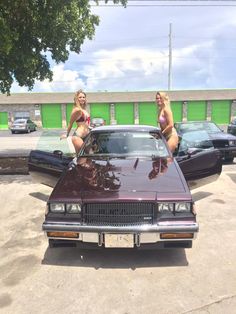 two women in bikinis sitting on the hood of a car with another woman standing next to it