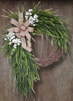 a wreath with white flowers and greenery on a wooden surface, tied with a brown ribbon