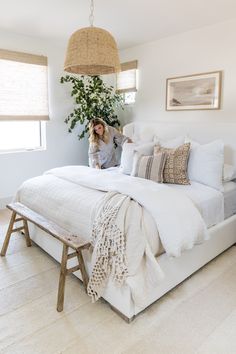 a woman standing in front of a bed with white linens