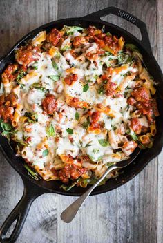 a skillet filled with pasta and sauce on top of a wooden table