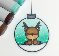 a christmas ornament with a reindeer in a snow globe on it and markers next to it