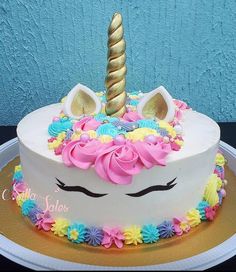 a white cake with pink, yellow and blue frosting has a unicorn horn on top