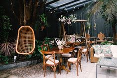 an outdoor dining area with wicker furniture and hanging plants in the back ground, surrounded by greenery