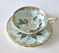 two tea cups and saucers decorated with flowers on blue, gold trimmings