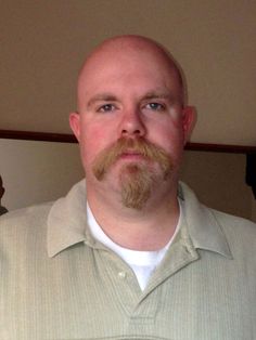 a bald man with a goatee and beard wearing a white shirt looking at the camera