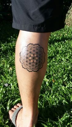 a man's leg with a flower of life tattoo on it, in the grass