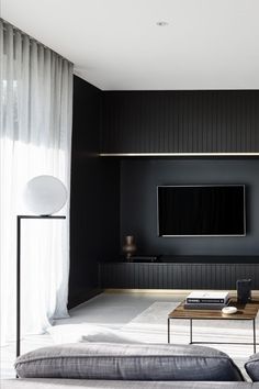 a modern living room with black walls and white carpeted flooring, large screen tv on the wall