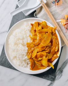 a white plate topped with chicken and rice next to chopsticks on a table