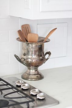 a silver pot with spoons and spatulas in it on a stove top