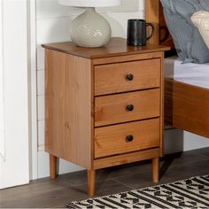 a nightstand with two drawers and a lamp on top of the night stand next to a bed