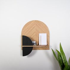 a wooden shelf with a book on it next to a potted plant and a white wall