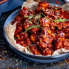 a blue bowl filled with meat covered in sauce and garnished with green onions