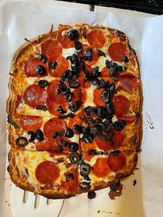 a pepperoni and black olive pizza on a cutting board with a spatula in it