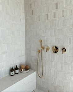 a white tiled shower with gold fixtures and soap dispensers on the wall