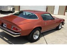 an orange muscle car parked in front of a garage with a trailer behind the car