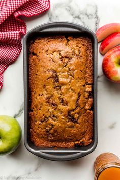 a loaf of apple cider bread in a pan next to apples and an orange juice