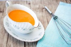 a bowl of soup on a saucer next to a whisk