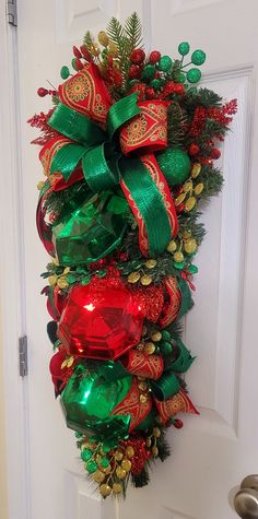 a christmas wreath on the front door decorated with red and green ribbons, pine cones, evergreens, and bells