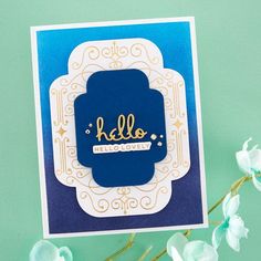 a blue and white card with the word hello written in gold on it, next to some flowers