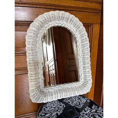 a white wicker mirror sitting on top of a black and white cushion next to a wooden door