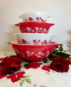 three red and white bowls with flowers on a tablecloth next to a rose flower