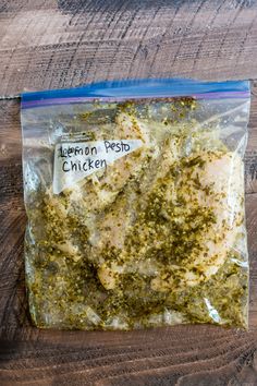 the chicken is covered with pesto and seasoning in a plastic bag on top of a wooden table