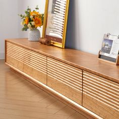 a wooden dresser with two pictures on it and a vase full of flowers next to it