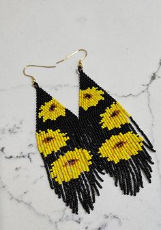 the black and yellow beaded earrings are hanging from gold hooks on a marble surface