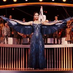 a woman standing on top of a stage wearing a blue dress with large birds flying around her