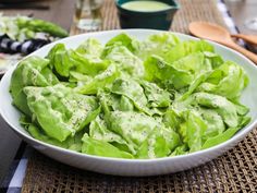 a white bowl filled with lettuce sitting on top of a table next to utensils