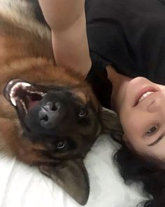 a woman laying next to a brown dog on top of a white blanket with her mouth open