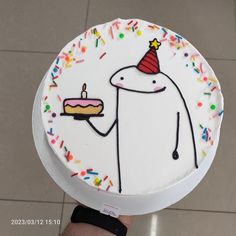 a hand holding a cake with sprinkles and a birthday hat on it